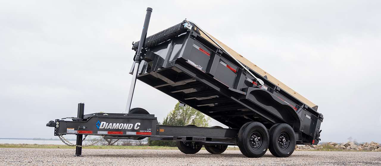 Tilted hydraulic dump trailer for rent against a bright sky - Hill Country Haulers serving Central Texas