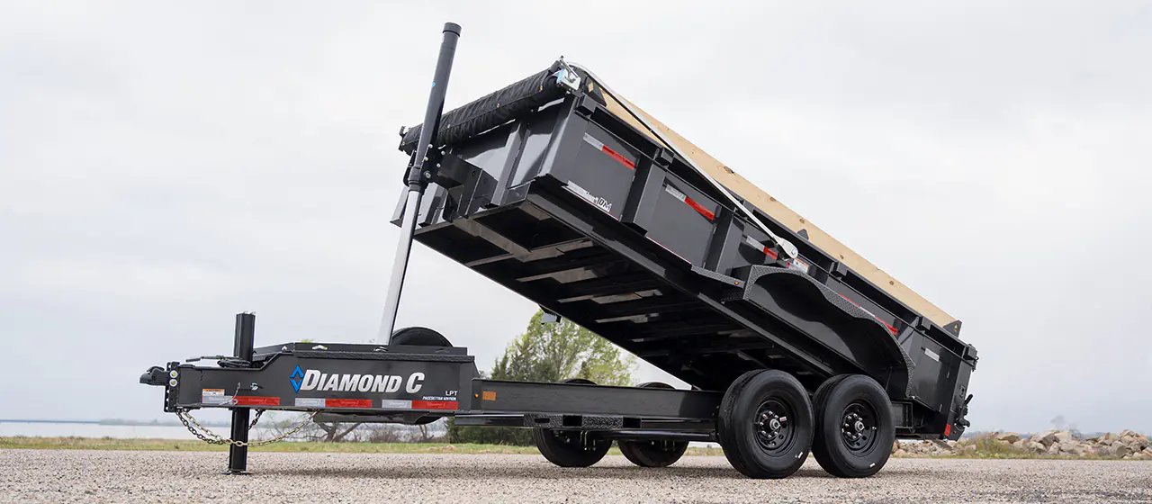 Tilted hydraulic dump trailer for rent against a bright sky - Hill Country Haulers serving Central Texas